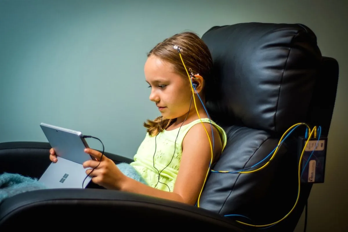 Enfant confortablement installé dans un fauteuil pendant une séance de neurofeedback, capteurs posés, tablette en mains